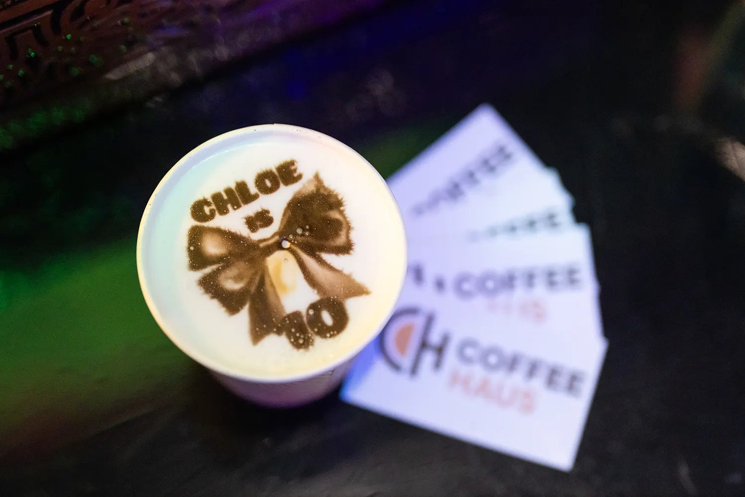 A cup of latte with foam art showing a bow and the words 